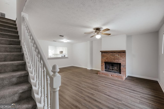 unfurnished living room with baseboards, dark wood-style floors, stairs, a textured ceiling, and a fireplace