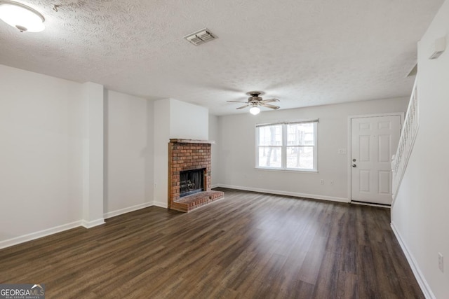 unfurnished living room featuring visible vents, dark wood-type flooring, a ceiling fan, a brick fireplace, and baseboards