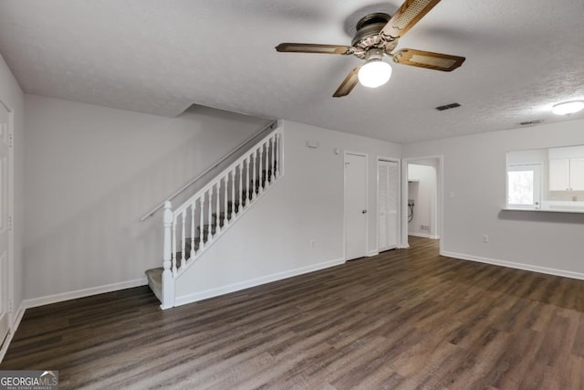 unfurnished living room with a textured ceiling, wood finished floors, visible vents, baseboards, and stairs