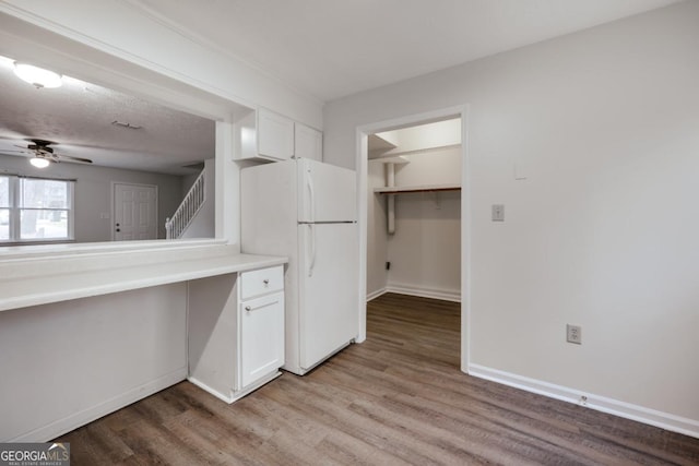 kitchen featuring light countertops, freestanding refrigerator, white cabinetry, light wood-type flooring, and baseboards