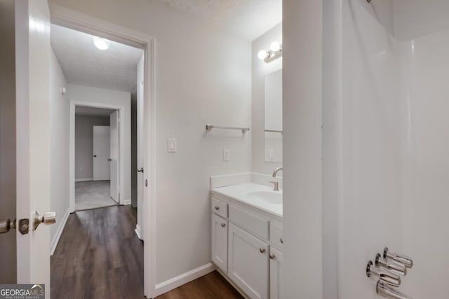 bathroom with baseboards, vanity, a textured ceiling, and wood finished floors