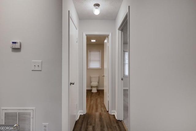 hallway with dark wood-style floors, baseboards, visible vents, and a textured ceiling