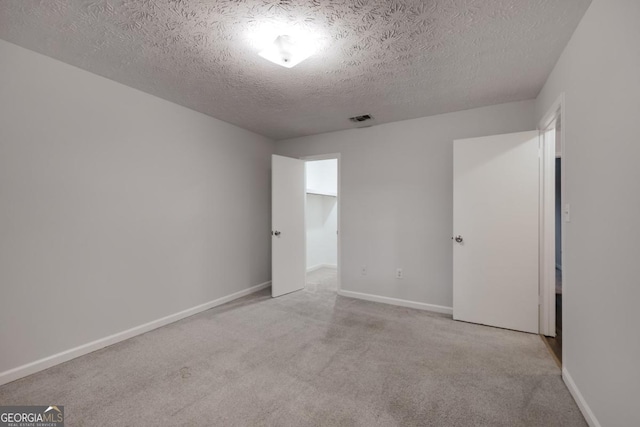 unfurnished bedroom featuring visible vents, light carpet, baseboards, and a textured ceiling