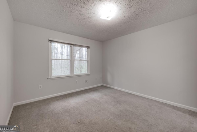 carpeted spare room featuring a textured ceiling and baseboards