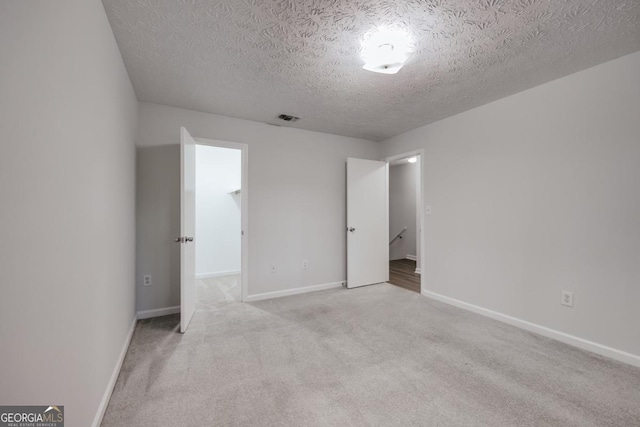 unfurnished bedroom with a walk in closet, light colored carpet, visible vents, a textured ceiling, and baseboards