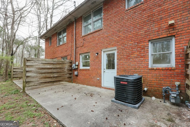 view of side of home featuring central air condition unit, fence, a patio, and brick siding