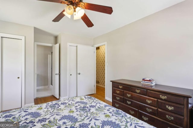 bedroom featuring multiple closets, wood finished floors, baseboards, and a ceiling fan