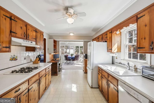 kitchen with crown molding, light countertops, a sink, white appliances, and under cabinet range hood