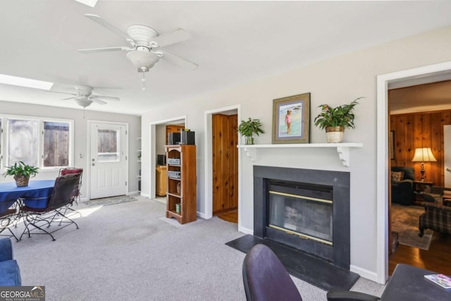 carpeted living room featuring a skylight, a glass covered fireplace, ceiling fan, and baseboards