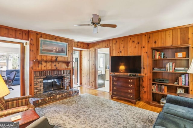 living area with ceiling fan, wood walls, a fireplace, wood finished floors, and ornamental molding