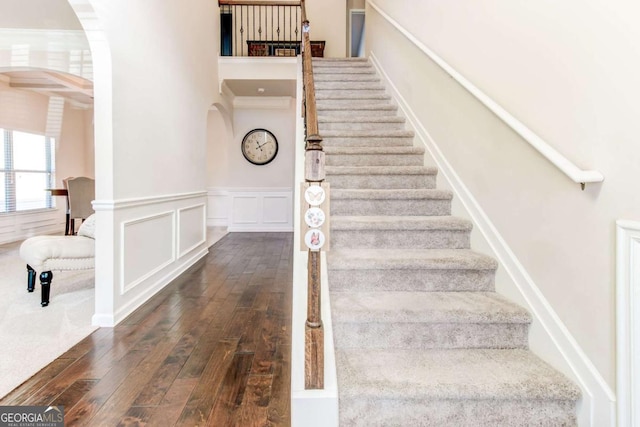 stairway featuring arched walkways, hardwood / wood-style floors, a wainscoted wall, and a decorative wall