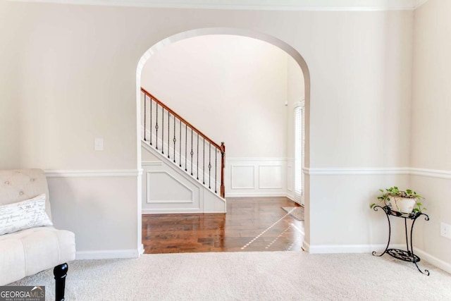 carpeted foyer featuring arched walkways, a decorative wall, stairway, and baseboards