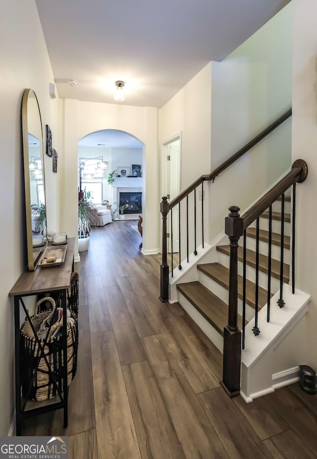 entryway with dark wood-type flooring, a glass covered fireplace, arched walkways, and stairway