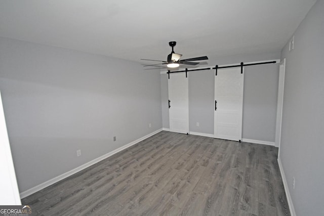 unfurnished bedroom with a barn door, wood finished floors, baseboards, and ceiling fan