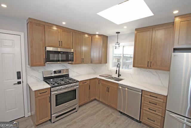 kitchen with light stone countertops, light wood-style flooring, a skylight, stainless steel appliances, and a sink