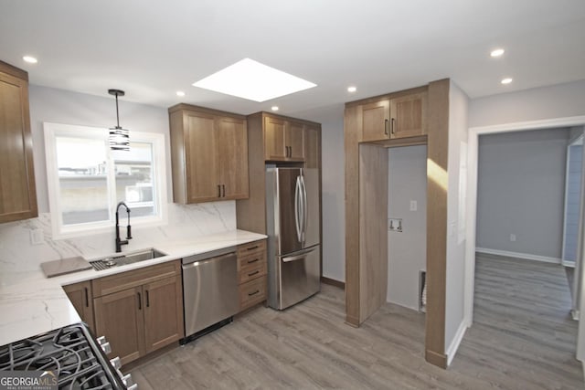 kitchen featuring a sink, stainless steel appliances, a skylight, light wood finished floors, and decorative backsplash