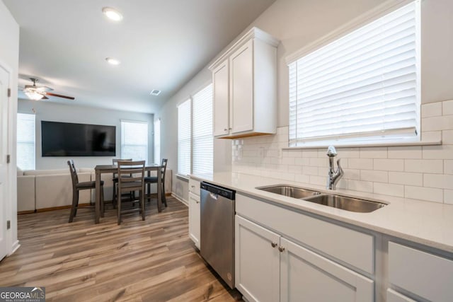 kitchen with light wood finished floors, backsplash, white cabinets, a sink, and dishwasher