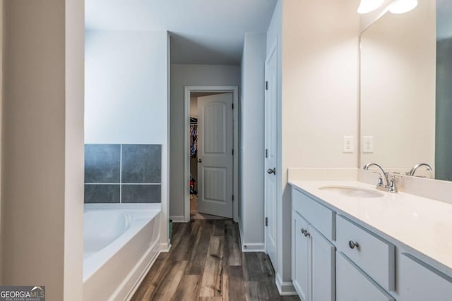 bathroom with a garden tub, wood finished floors, vanity, baseboards, and a walk in closet