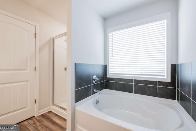 bathroom with a stall shower, wood finished floors, and a bath