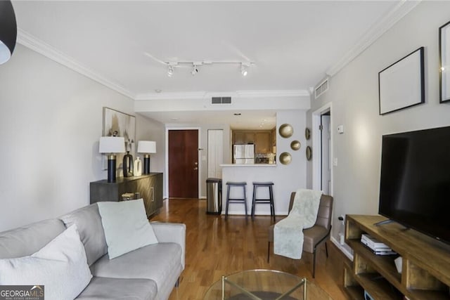 living area with track lighting, visible vents, wood finished floors, and ornamental molding