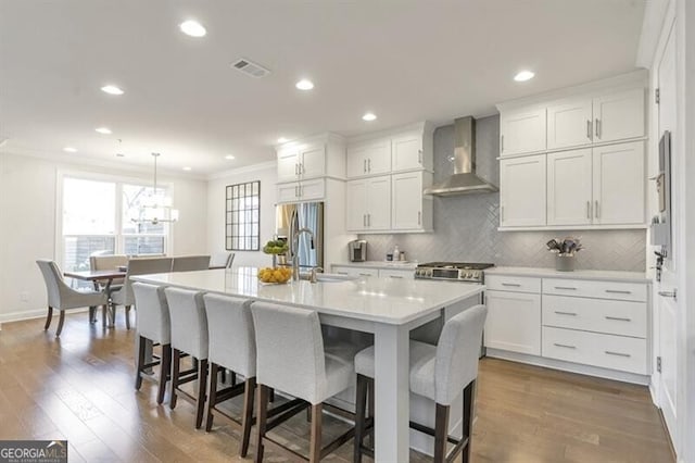 kitchen with crown molding, visible vents, white cabinetry, a sink, and wall chimney exhaust hood