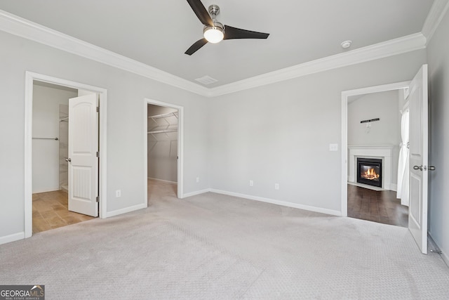 unfurnished bedroom featuring carpet, baseboards, ornamental molding, a spacious closet, and a glass covered fireplace