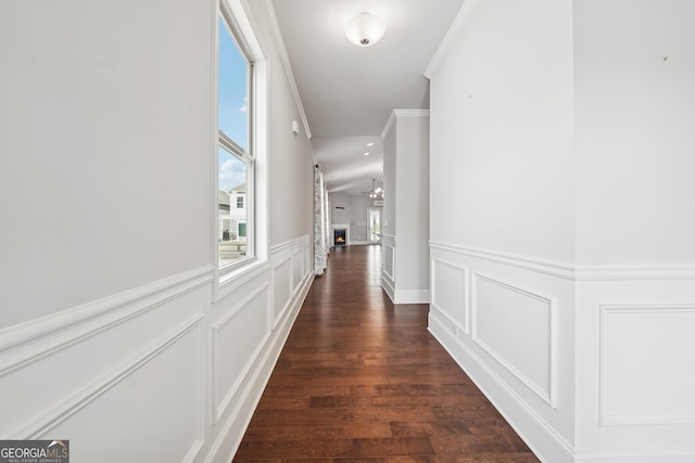 hall with crown molding, dark wood-type flooring, wainscoting, an inviting chandelier, and a decorative wall