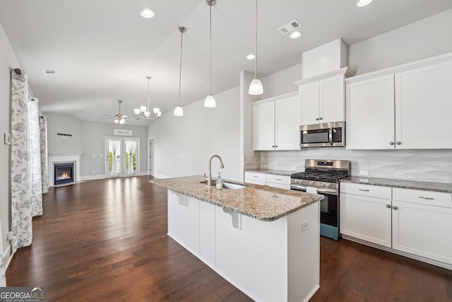 kitchen featuring visible vents, a sink, backsplash, a glass covered fireplace, and appliances with stainless steel finishes