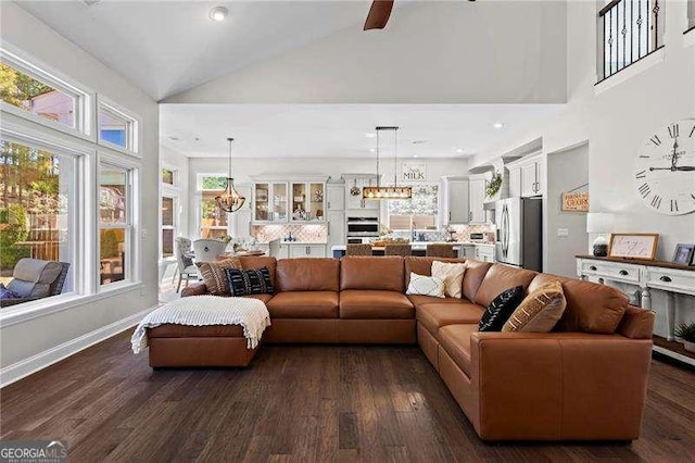 living room with baseboards, dark wood-style flooring, ceiling fan with notable chandelier, high vaulted ceiling, and recessed lighting