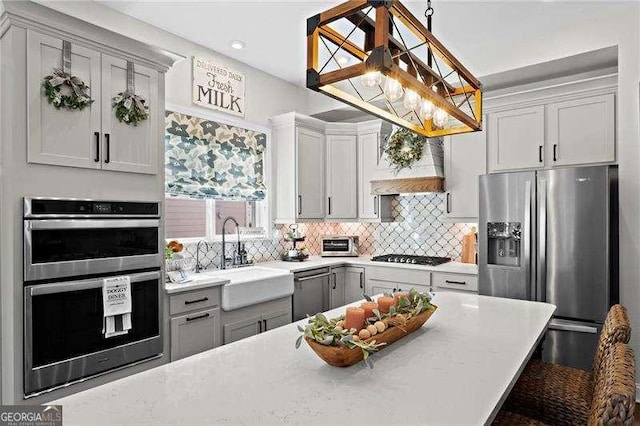 kitchen with stainless steel appliances, light countertops, custom range hood, decorative backsplash, and a sink