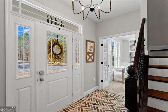 foyer entrance with stairs, brick floor, a chandelier, and baseboards