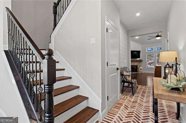 stairway featuring brick floor, a brick fireplace, ceiling fan, and baseboards