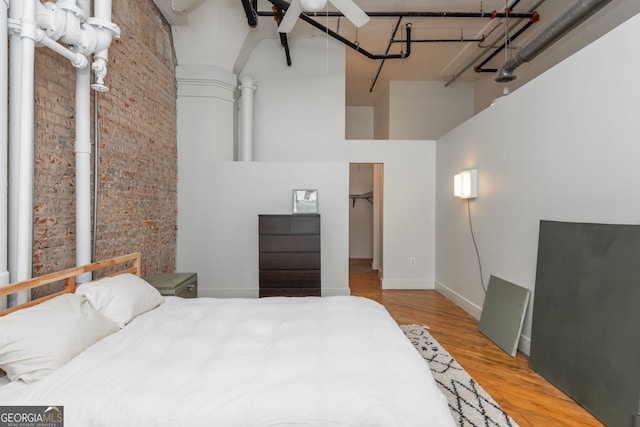 bedroom featuring wood finished floors, baseboards, brick wall, a towering ceiling, and a walk in closet