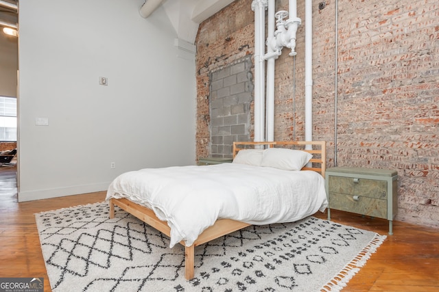 bedroom featuring baseboards, wood finished floors, and brick wall