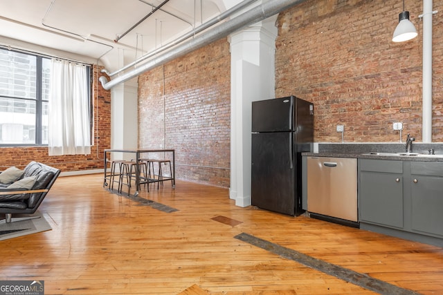 kitchen featuring light wood finished floors, brick wall, freestanding refrigerator, a sink, and stainless steel dishwasher