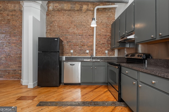 kitchen with brick wall, light wood finished floors, a sink, under cabinet range hood, and appliances with stainless steel finishes