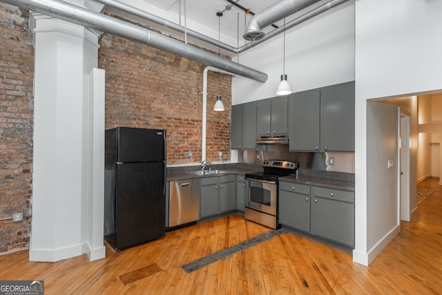 kitchen with a sink, gray cabinetry, stainless steel appliances, a towering ceiling, and dark countertops