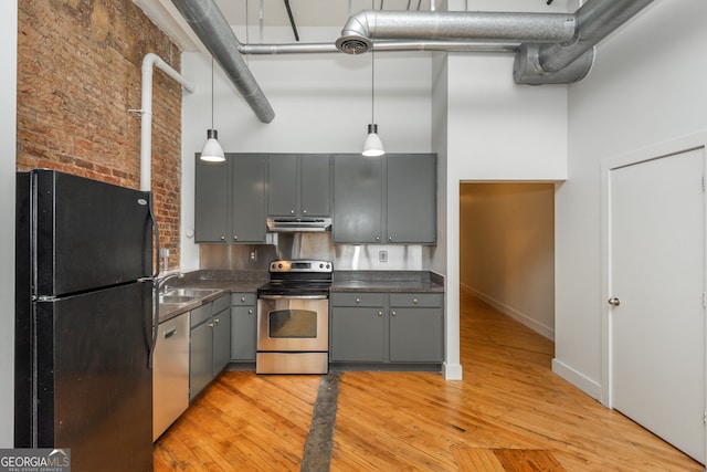 kitchen featuring dark countertops, gray cabinets, light wood-style flooring, a towering ceiling, and stainless steel appliances