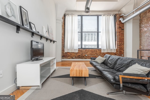 living area with brick wall, baseboards, and wood finished floors