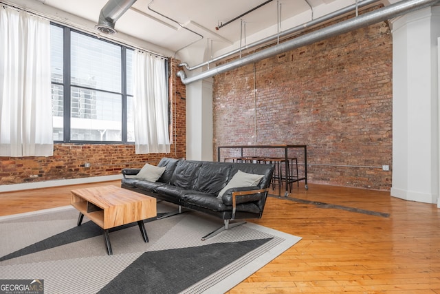 living room featuring a high ceiling, wood-type flooring, and brick wall