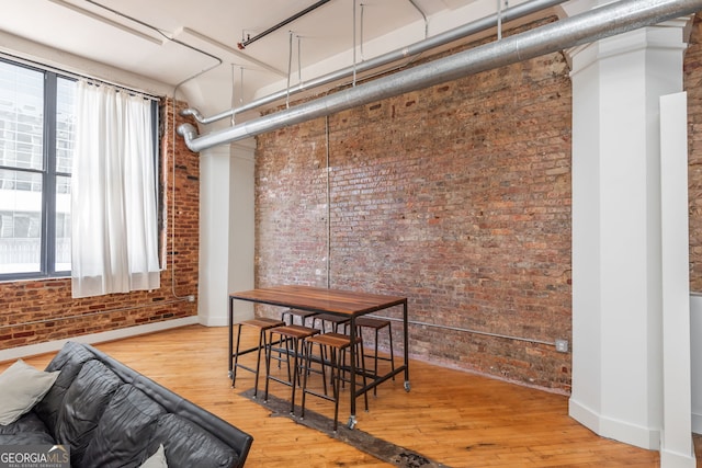 dining space featuring wood finished floors, a healthy amount of sunlight, and brick wall