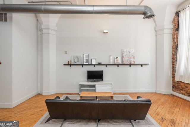 living area featuring baseboards, hardwood / wood-style flooring, and ornate columns