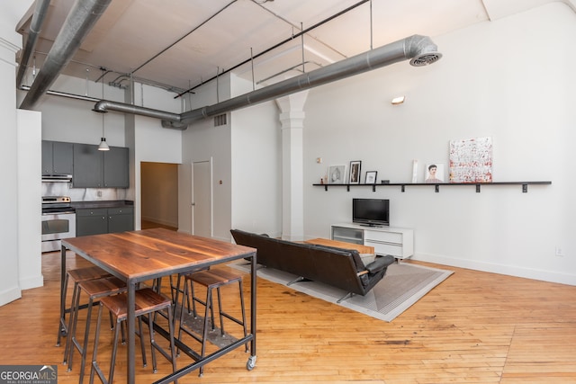 kitchen featuring visible vents, light wood-style flooring, under cabinet range hood, stainless steel range with electric cooktop, and a high ceiling