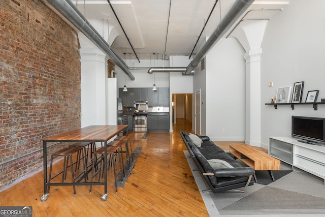 living area with brick wall, baseboards, decorative columns, light wood-style flooring, and a high ceiling