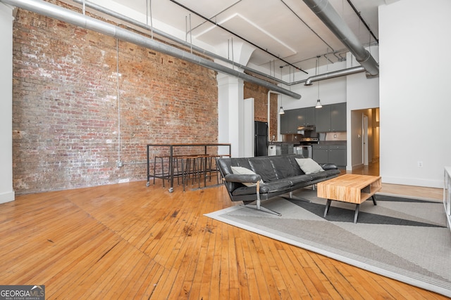 living area with light wood-style flooring, baseboards, a towering ceiling, and brick wall