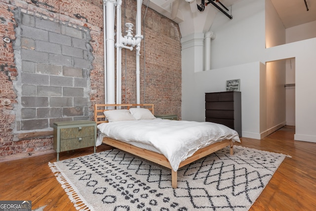 bedroom with baseboards, wood finished floors, a towering ceiling, and brick wall