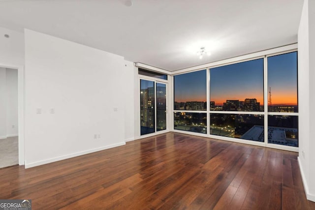 empty room with a wall of windows, baseboards, a city view, and hardwood / wood-style floors