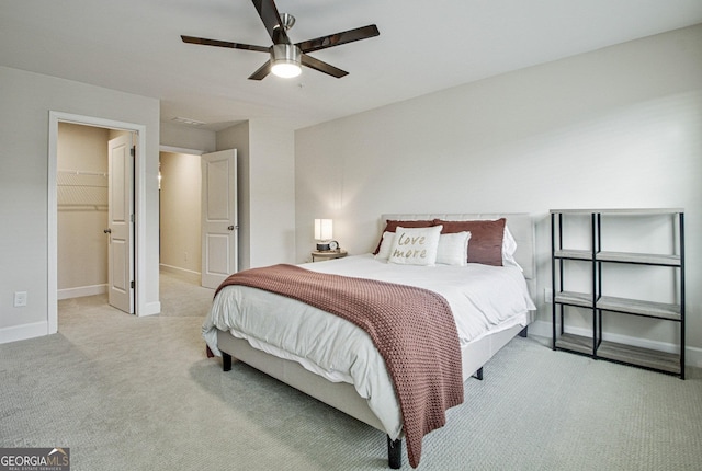 bedroom featuring light carpet, ceiling fan, a spacious closet, and baseboards