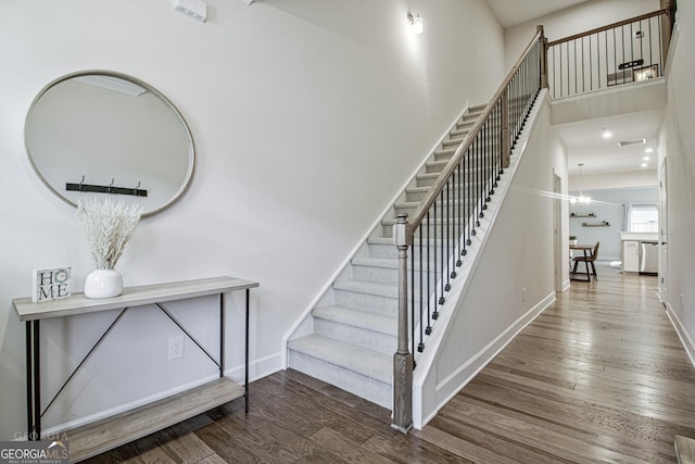 stairway with a chandelier, wood finished floors, visible vents, and baseboards