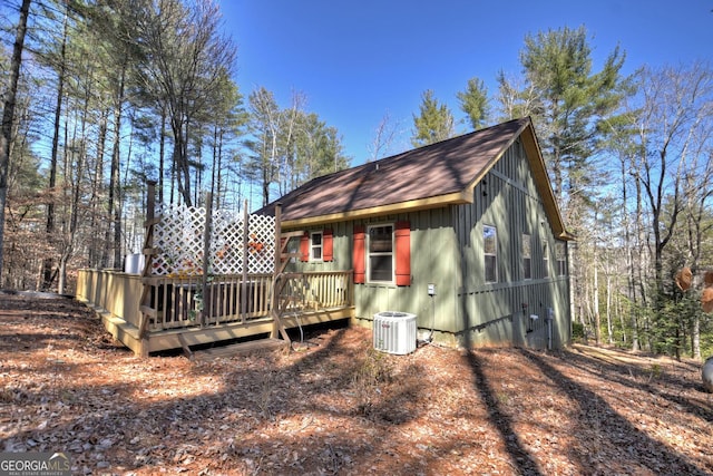 rear view of house with a shingled roof, a wooden deck, and central AC unit